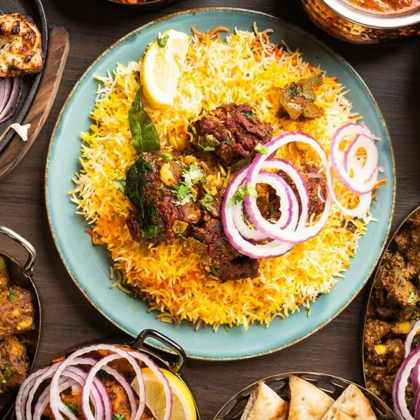 A vibrant spread of Indian dishes, including biryani, curries, and grilled meats, garnished with onions and lemon.
