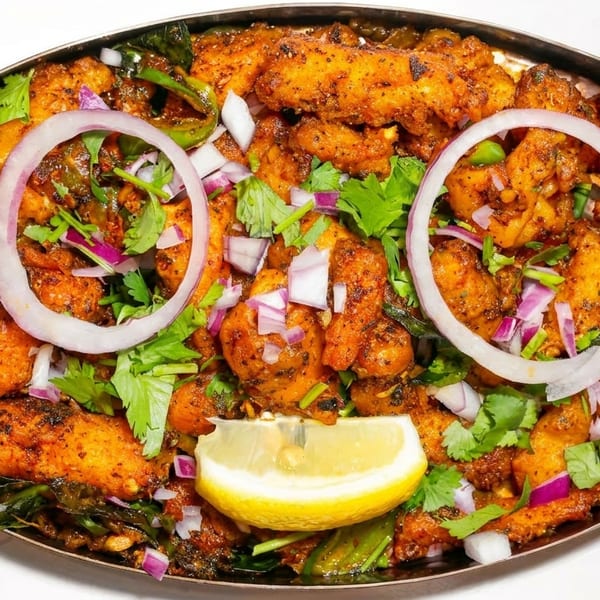 Spicy fried chicken pieces garnished with red onion rings, cilantro, and a lemon wedge.
