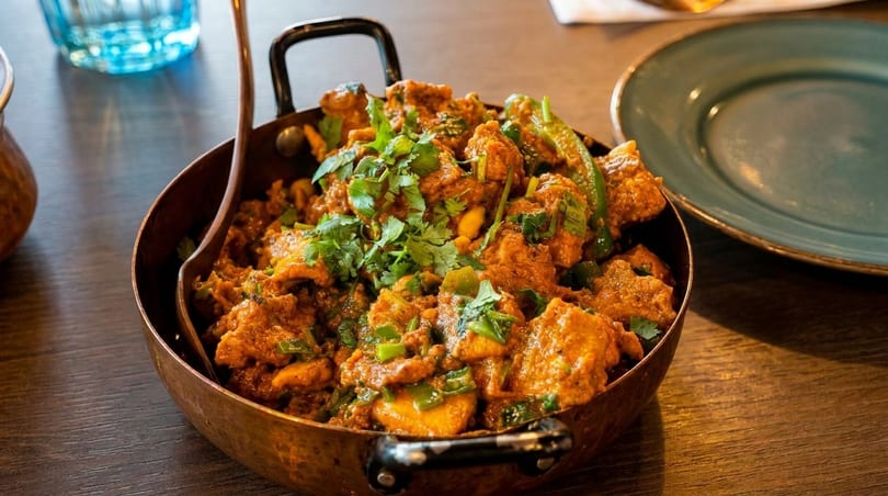Indian curry with chicken, green peppers, and cilantro in a copper bowl on a wooden table.