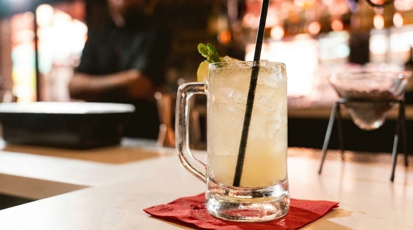 Iced cocktail with a lemon slice and mint sprig on a red napkin at a bar.