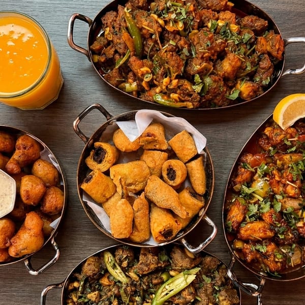 Overhead view of five copper bowls filled with various Indian dishes and a glass of mango juice.