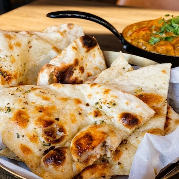 A basket of garlic naan bread with a side of chicken tikka masala on a wooden table.