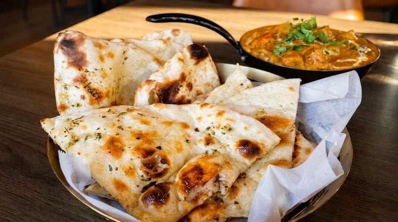 A basket of garlic naan bread with a side of chicken tikka masala on a wooden table.