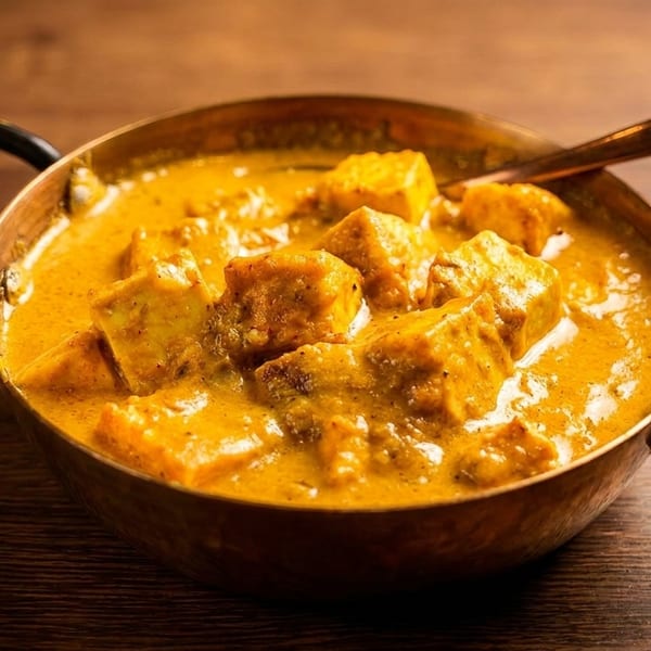 Paneer butter masala, an Indian curry dish, in a copper serving bowl with a spoon.