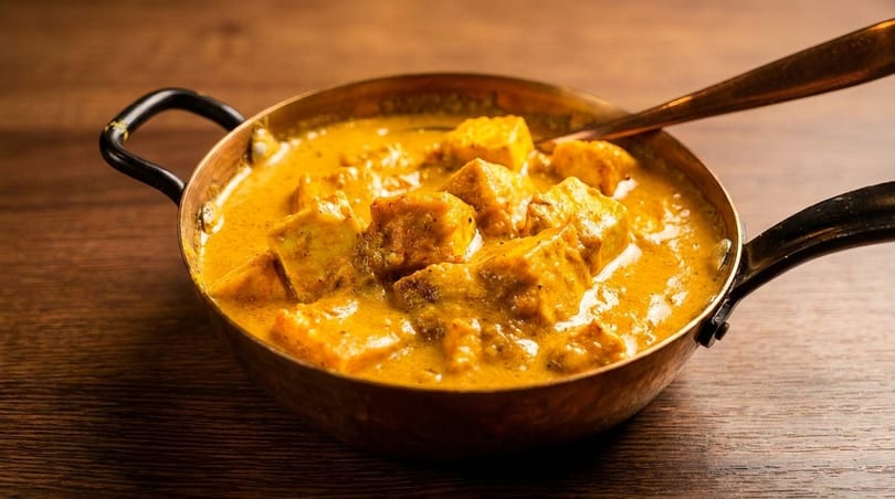Paneer butter masala, an Indian curry dish, in a copper serving bowl with a spoon.